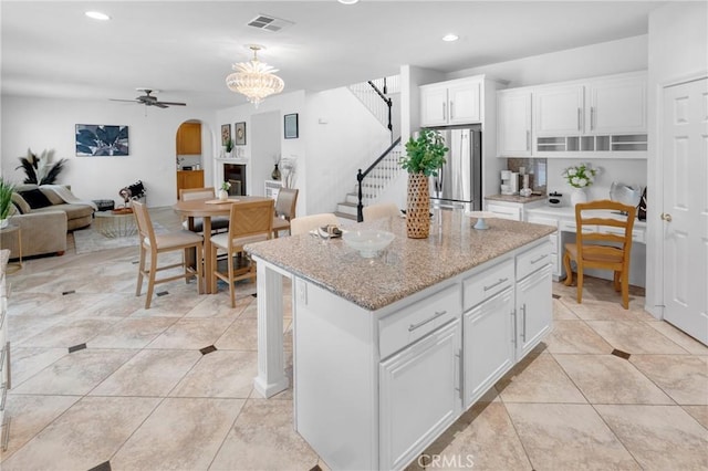 kitchen featuring arched walkways, ceiling fan with notable chandelier, freestanding refrigerator, white cabinetry, and visible vents