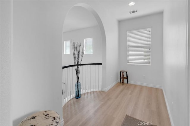 interior space with arched walkways, baseboards, visible vents, and light wood-style flooring