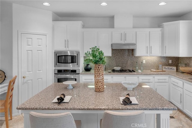 kitchen with a kitchen island, under cabinet range hood, white cabinets, and stainless steel appliances