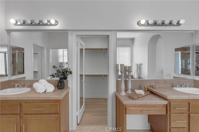 full bathroom featuring tile patterned flooring, a sink, a stall shower, and two vanities