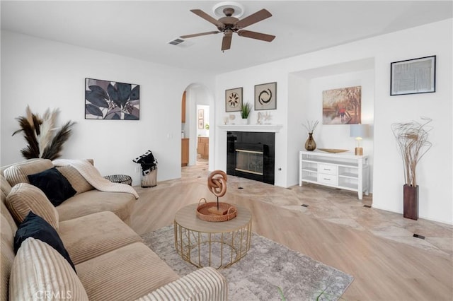 living area with visible vents, a ceiling fan, wood finished floors, a fireplace, and arched walkways