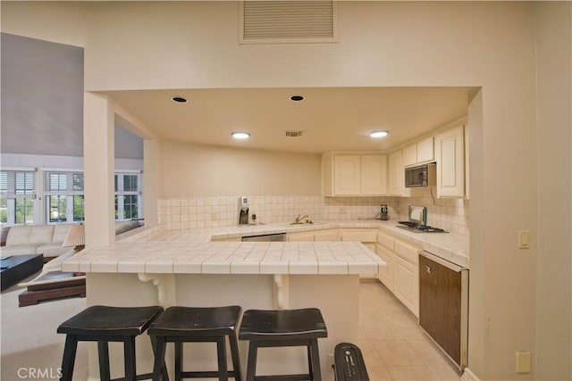 3155 Stone Oak Dr, Los Angeles, CA 90049 - kitchen with tasteful backsplash, stainless steel appliances, tile counters, visible vents, and a peninsula