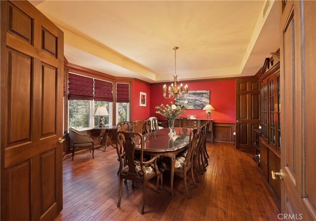 3155 Stone Oak Dr, Los Angeles, CA 90049 - dining space with dark wood-style floors, a raised ceiling, an inviting chandelier, and a wainscoted wall