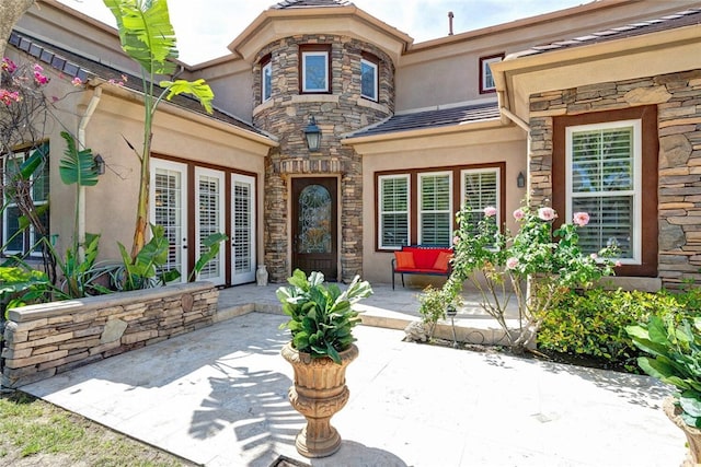 view of exterior entry with stucco siding, a patio area, and stone siding