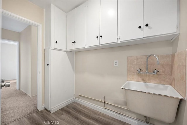 clothes washing area with a sink, wood finished floors, and baseboards