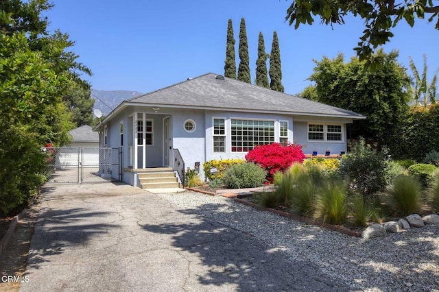 bungalow with a gate, fence, stucco siding, and roof with shingles