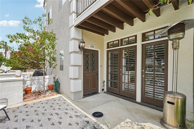view of exterior entry with fence, stucco siding, french doors, and a patio area