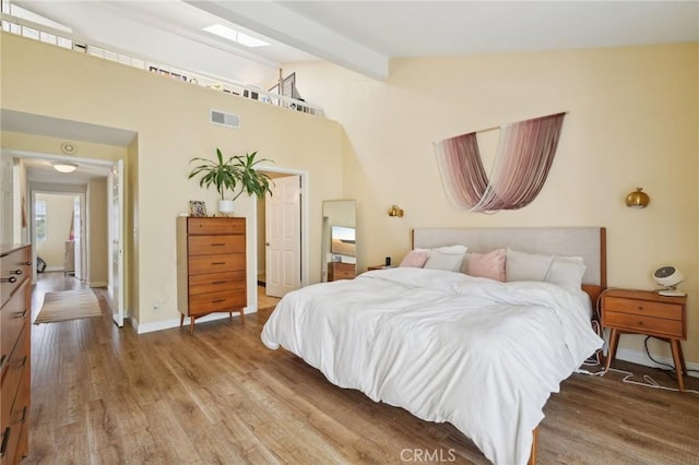 bedroom featuring baseboards, visible vents, lofted ceiling with beams, and wood finished floors