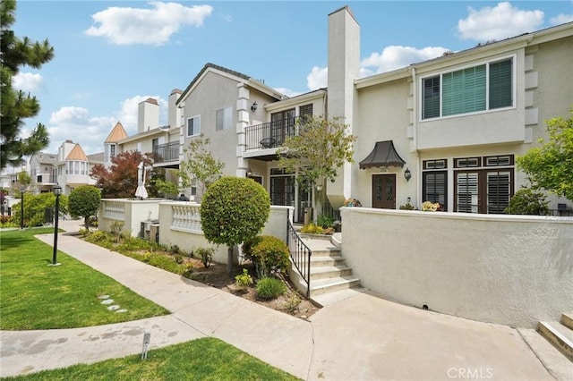 townhome / multi-family property with a balcony, a residential view, a chimney, a front yard, and stucco siding