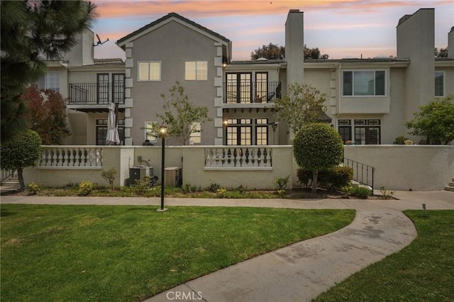 back of property at dusk featuring stucco siding, a chimney, a lawn, and a balcony