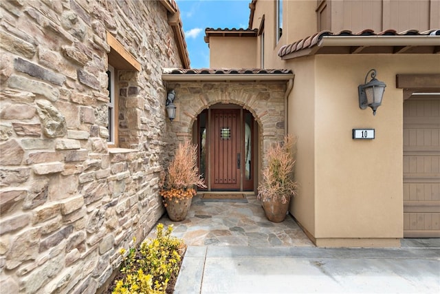 property entrance featuring stucco siding, a tiled roof, and stone siding
