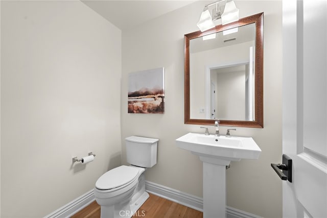 half bath featuring visible vents, wood finished floors, toilet, baseboards, and a sink
