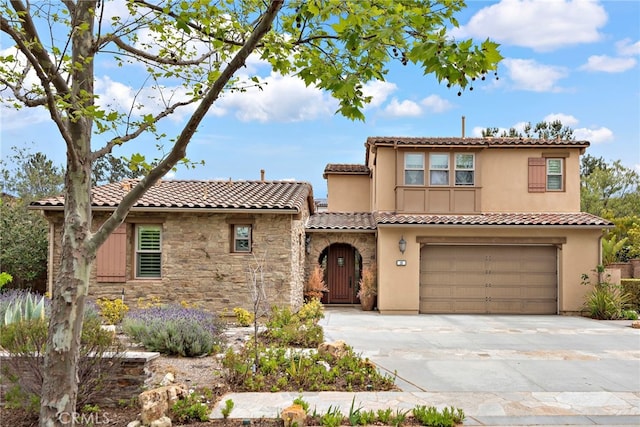 mediterranean / spanish-style home featuring an attached garage, concrete driveway, a tiled roof, and stone siding