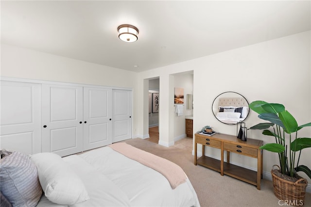 bedroom featuring light colored carpet, baseboards, ensuite bathroom, and a closet