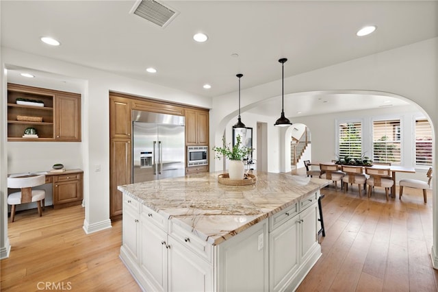 kitchen featuring light stone countertops, light wood-style floors, built in appliances, arched walkways, and visible vents