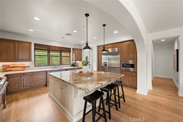 kitchen featuring a sink, built in appliances, brown cabinetry, a center island, and visible vents