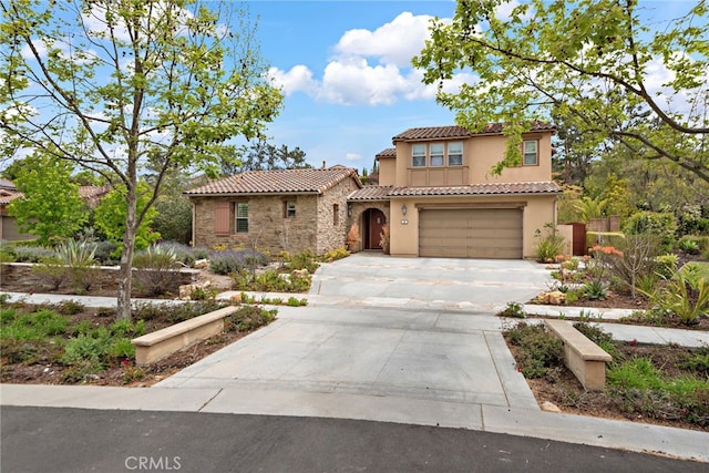mediterranean / spanish house with stone siding, a garage, stucco siding, concrete driveway, and a tiled roof