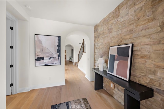 hallway featuring baseboards, arched walkways, stairs, and wood finished floors