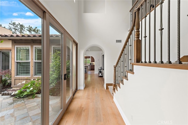 foyer entrance with visible vents, arched walkways, light wood-style flooring, and a wealth of natural light