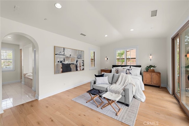 bedroom with light wood-style floors, arched walkways, baseboards, lofted ceiling, and visible vents