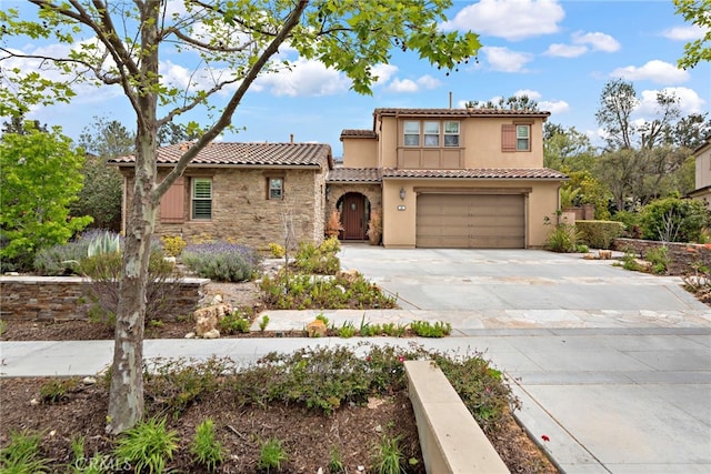 mediterranean / spanish house featuring a tile roof, stone siding, a garage, stucco siding, and concrete driveway
