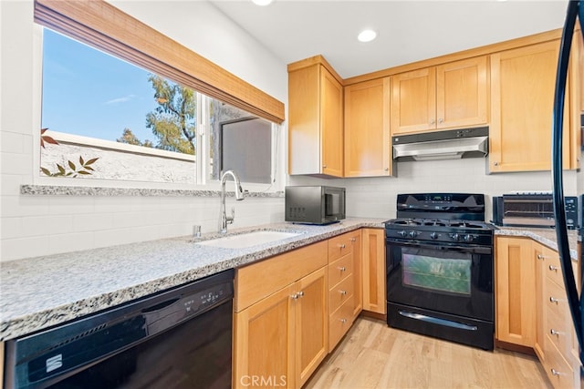 kitchen with a sink, light wood finished floors, tasteful backsplash, under cabinet range hood, and black appliances