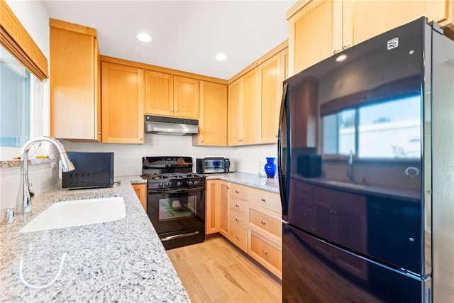kitchen featuring light brown cabinets, under cabinet range hood, a sink, backsplash, and black appliances