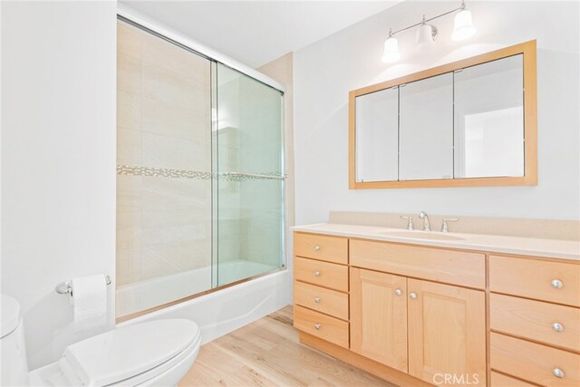 bathroom with toilet, wood finished floors, shower / bath combination with glass door, and vanity