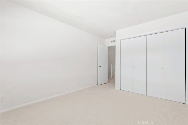 unfurnished bedroom with baseboards, a closet, and light colored carpet