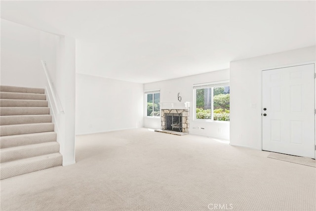 unfurnished living room featuring carpet flooring, a fireplace, and stairway