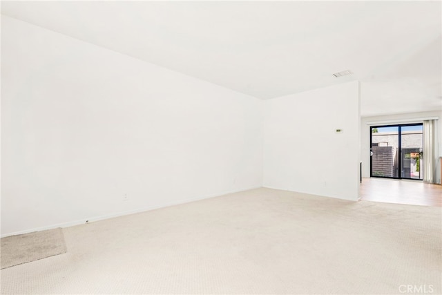 empty room featuring baseboards, light carpet, and visible vents