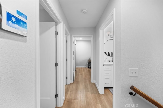 hall with light wood-type flooring, a sink, a textured wall, and baseboards
