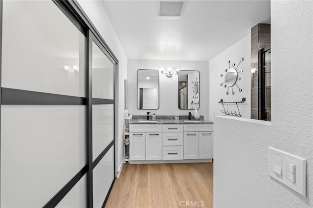 full bathroom with double vanity, a sink, wood finished floors, and visible vents