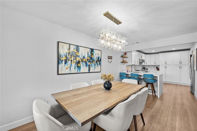 dining area with light wood-style floors, a textured ceiling, baseboards, and a chandelier