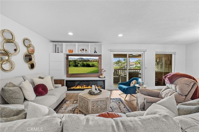 living area with recessed lighting, a glass covered fireplace, and wood finished floors