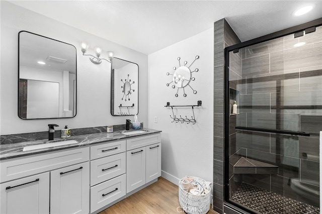 bathroom featuring double vanity, a sink, a stall shower, and wood finished floors