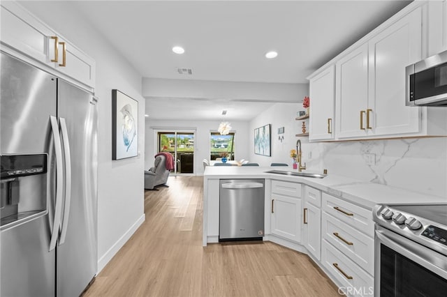 kitchen with appliances with stainless steel finishes, a sink, a peninsula, light wood finished floors, and white cabinetry