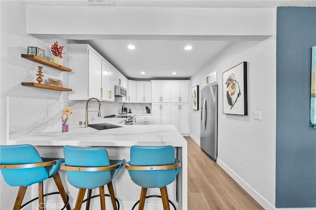 kitchen with a peninsula, light wood-style floors, light stone counters, a sink, and appliances with stainless steel finishes