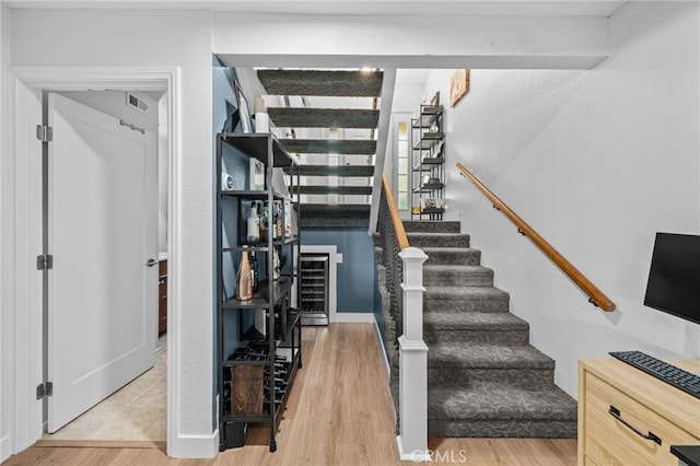 stairs with wine cooler, wood finished floors, and visible vents
