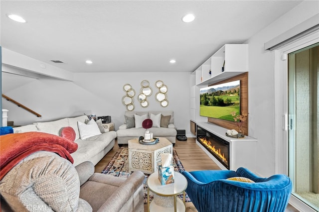 living area with recessed lighting, a glass covered fireplace, wood finished floors, and visible vents