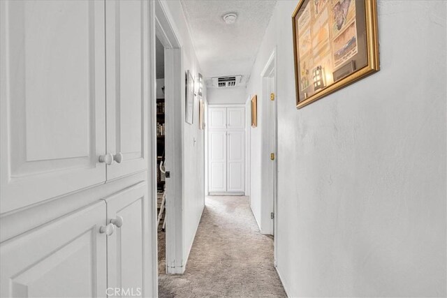 corridor with a textured ceiling, visible vents, and light carpet