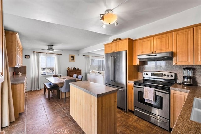 kitchen featuring tasteful backsplash, appliances with stainless steel finishes, a center island, under cabinet range hood, and dark tile patterned floors