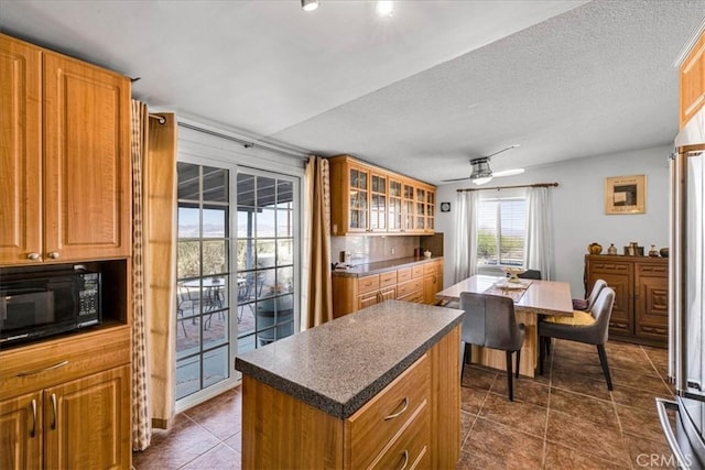 kitchen featuring dark countertops, black microwave, a ceiling fan, and a kitchen island