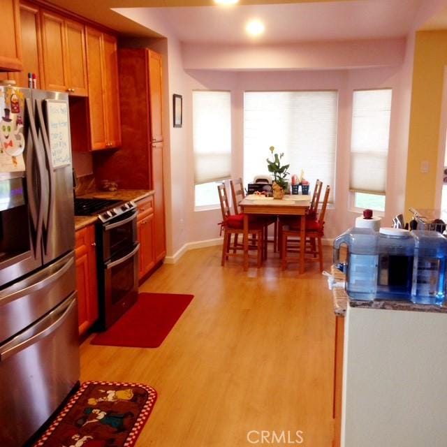 kitchen featuring recessed lighting, light wood-style floors, brown cabinetry, baseboards, and appliances with stainless steel finishes