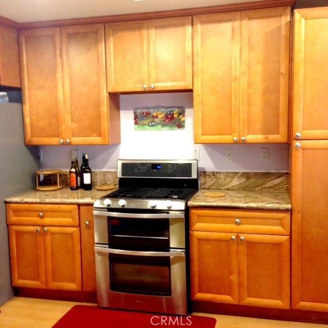 kitchen featuring light wood-style flooring, double oven range, light stone counters, and brown cabinetry