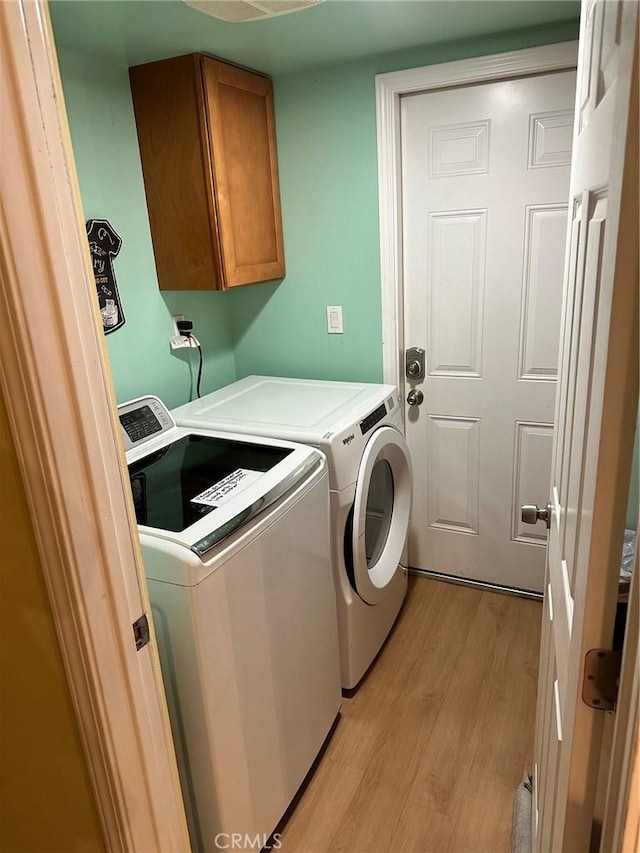 washroom with cabinet space, washing machine and clothes dryer, and light wood-style flooring