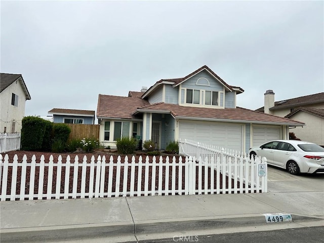 traditional home featuring driveway, a garage, a fenced front yard, and a tiled roof