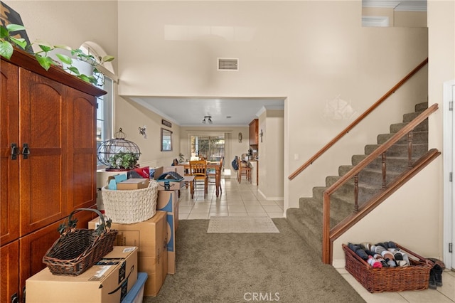 foyer featuring crown molding, stairway, light tile patterned flooring, light carpet, and a towering ceiling
