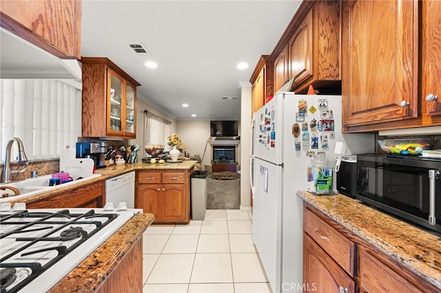kitchen with light tile patterned floors, glass insert cabinets, brown cabinetry, visible vents, and white appliances
