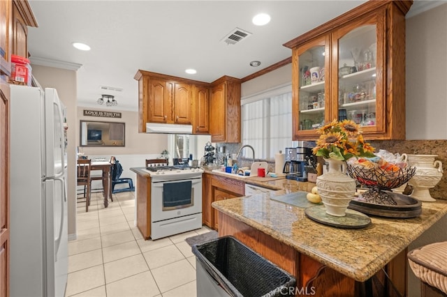 kitchen with crown molding, a peninsula, under cabinet range hood, and white appliances